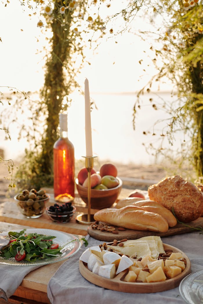 Serene outdoor picnic setup with cheese, wine, and breads on a rustic table at sunset.